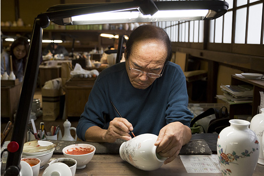 文様の線描きや色を塗る作業を行う「絵書座（えかきざ）」。一瞬の筆の乱れでそれまでの工程が台無しになってしまうため、職人たちは緊張の表情で筆を動かす。室内の張り詰めた空気が息苦しいほどだ。