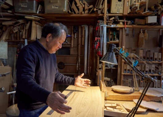 木取りについて説明する宮本氏。写真の材の木目をどのように見せるか、どこから切るかで、制作可能な作品が変わってくる。