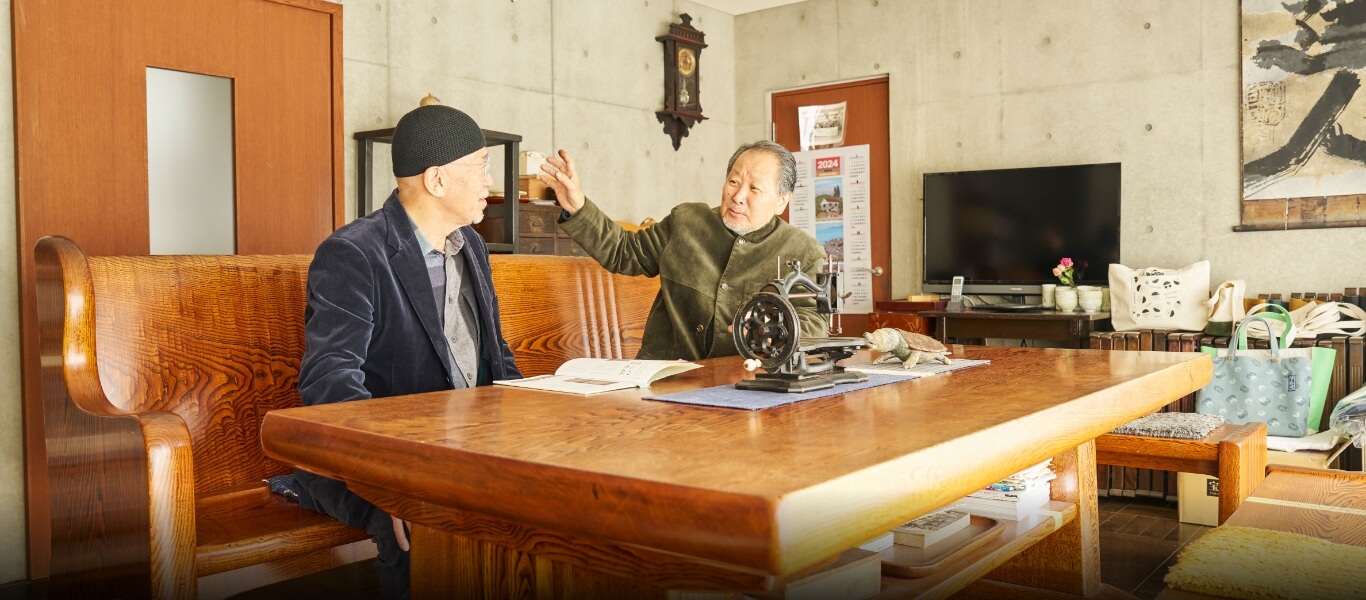 2008年制作の栗材の応接セットで一澤信三郎氏と。テーブルの脚や背もたれに刻まれた意匠、華やかな杢目の見せ方などに宮本氏らしさがあふれている。
