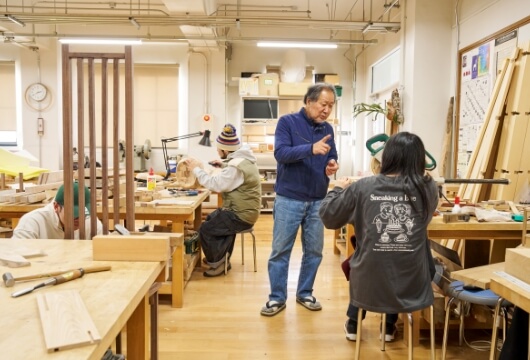 京都美術工芸大学で卒業制作を指導する様子。教え子たちの主な就職先は木工関係の企業である。宮本氏の背中を追うように、木工芸作家として活動している卒業生もいる。