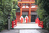 「氷川神社」の楼門（ろうもん）へ向かう巫女。朱色が境内の緑に鮮やかに映える。