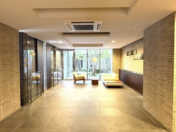 ガラスウォールから屋外の緑を望むロビー空間。共用部には不在時に役立つ宅配ボックスが備わっています。