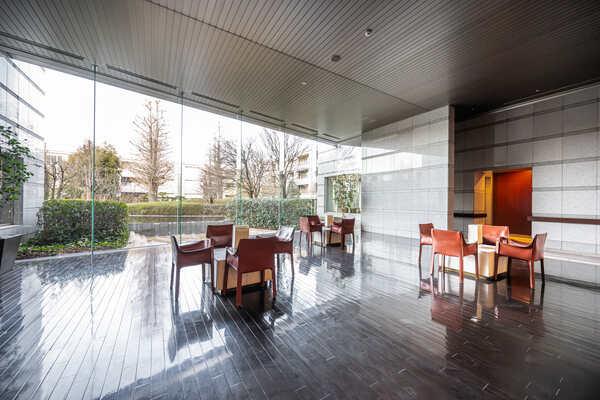 テーブルセットが配されたロビー。ガラスウォールから樹々の風景が広がり、陽光差し込む明るい空間です。