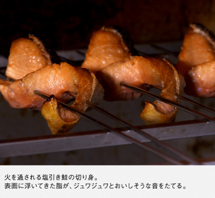 火を通される塩引き鮭の切り身。表面に浮いてきた脂が、ジュワジュワとおいしそうな音をたてる。